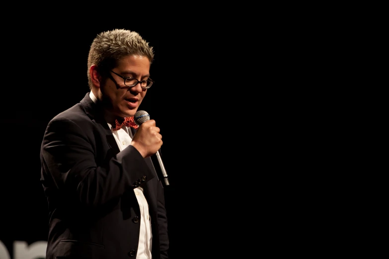 a man wearing glasses holds a microphone while talking