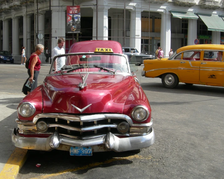 a red vintage car is parked in front of the taxi