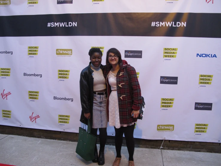 two women standing together in front of a backdrop