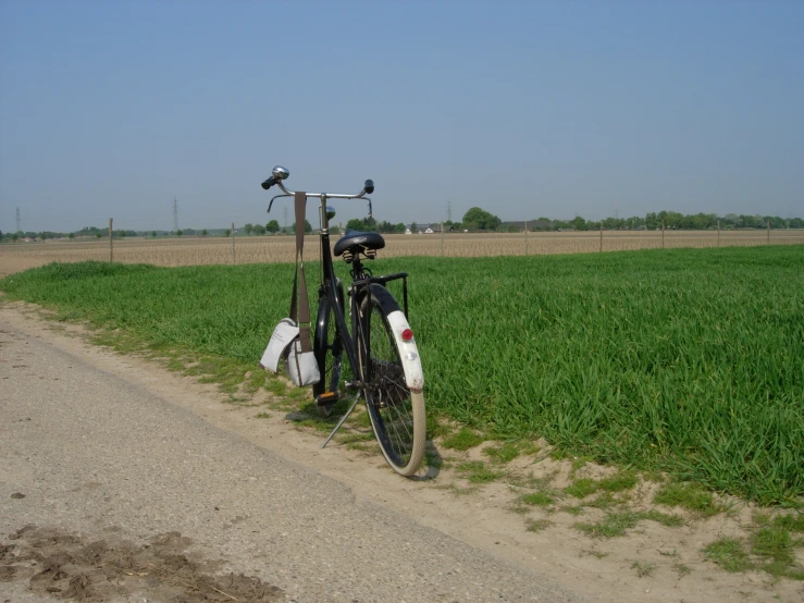 a bicycle parked on the side of a dirt road next to a field