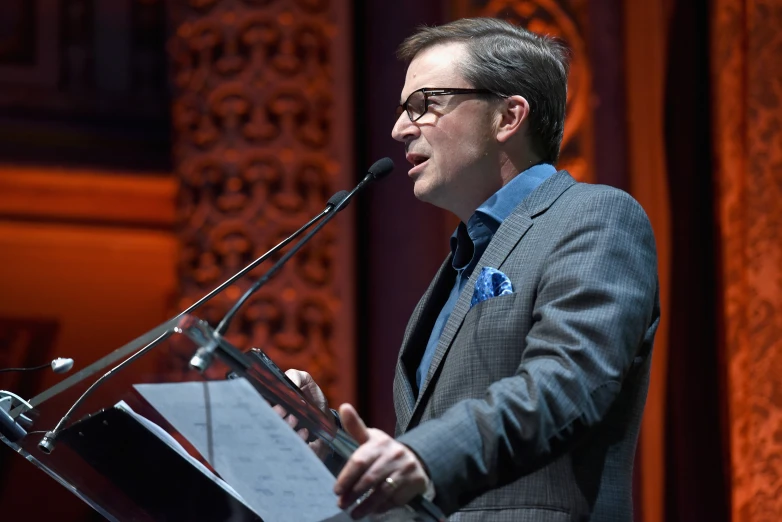 a man wearing glasses standing at a microphone