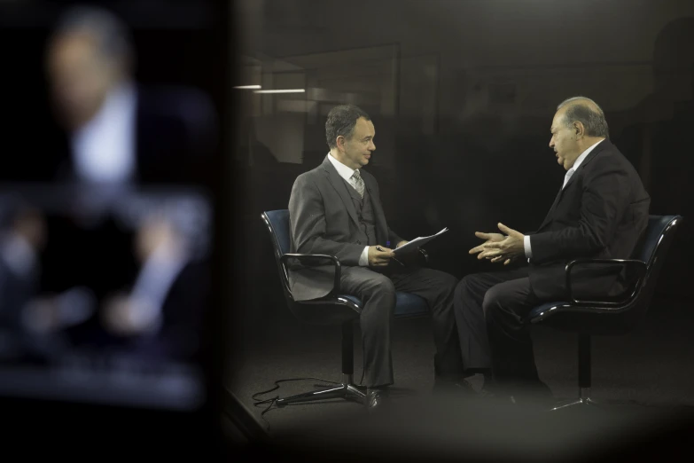 two men sitting in chairs talking to each other