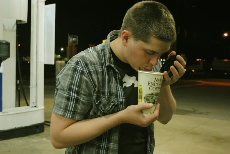 young man sipping coffee from coffee cup in front of gas pump