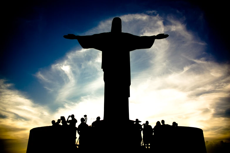 silhouetted people standing at the base of a statue