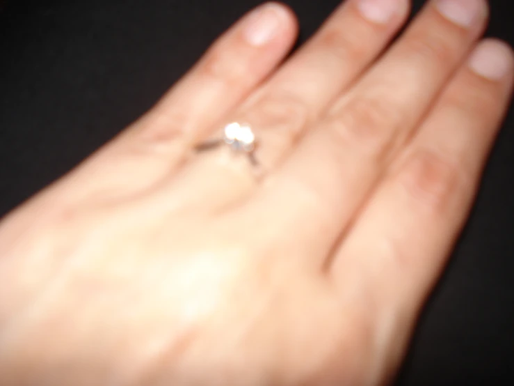 a person with one hand holding a white engagement ring