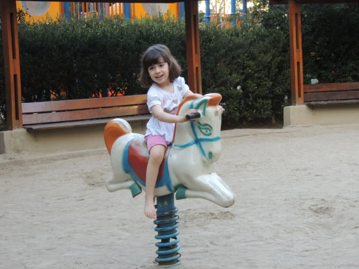 a little girl rides a playground horse at the park