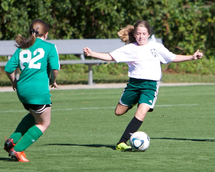 three young women playing soccer against each other on a field