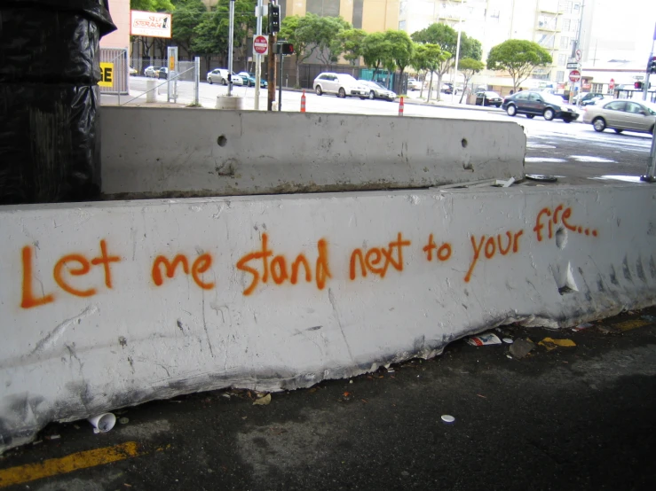 a street lined with tall buildings and graffiti that reads let me stay next to your fire