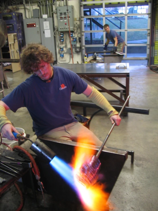 a man sitting in a glass factory working on an object with orange flames