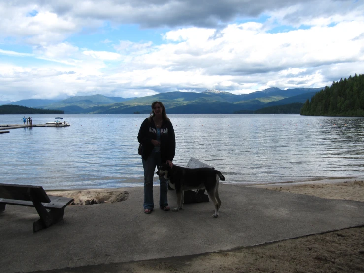 a woman and two dogs standing next to each other near a lake