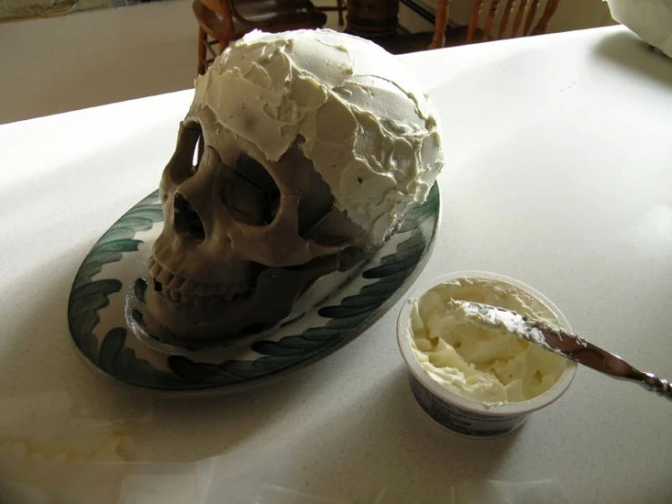 a skull cake sits on a plate next to the bowl of whipped cream