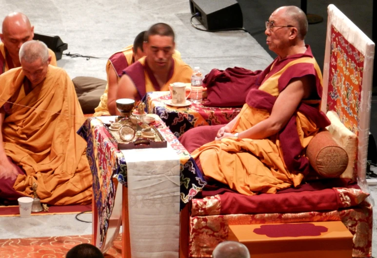 some monks are sitting around with cups and food