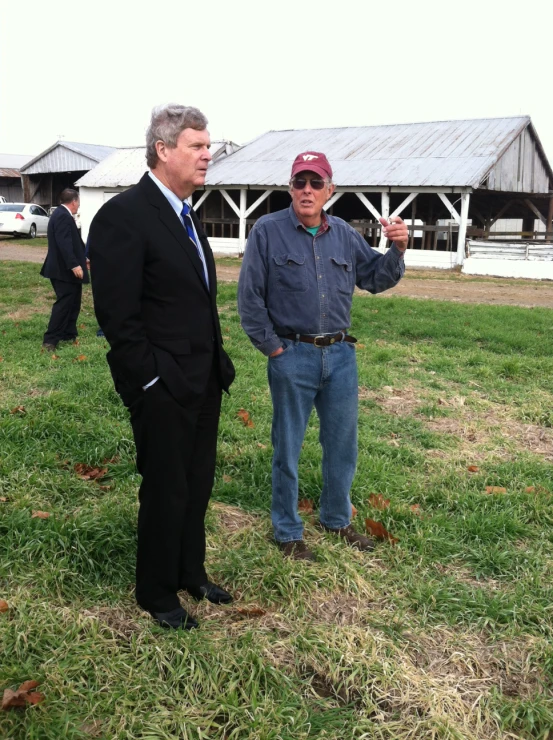 two men talking next to each other in front of a barn