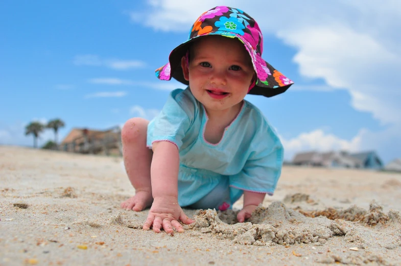 a baby on a beach laying down wearing a hat