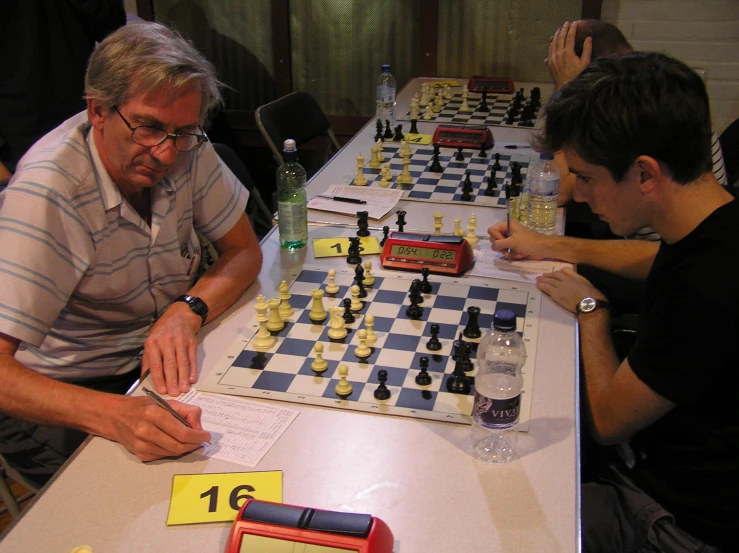 three men playing chess on a boardgame with a notepad