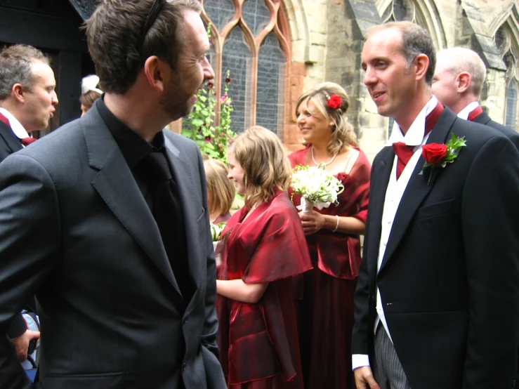 a couple dressed in dark red and a man wearing a black suit