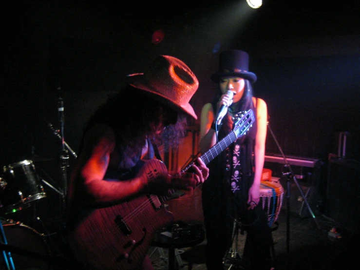 two musicians, one dressed in black playing guitar and the other singing