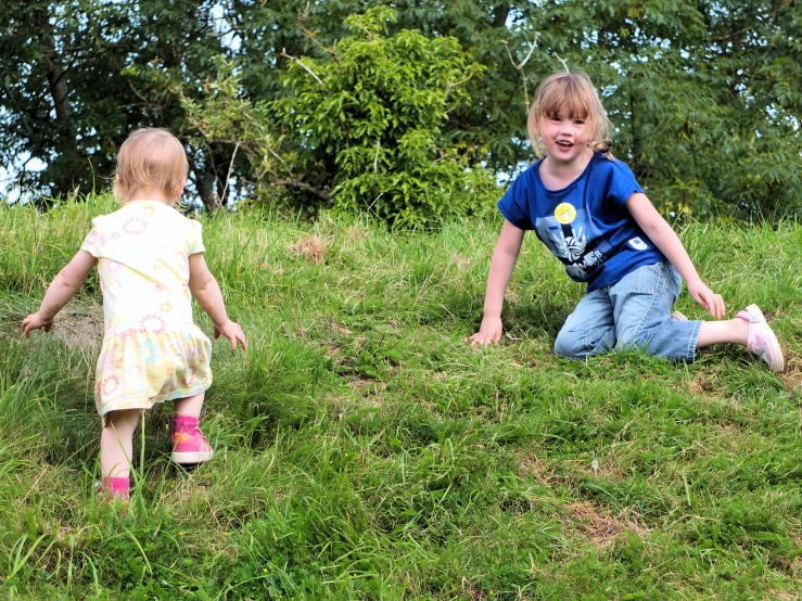 a couple of young children standing on top of a grass covered hillside