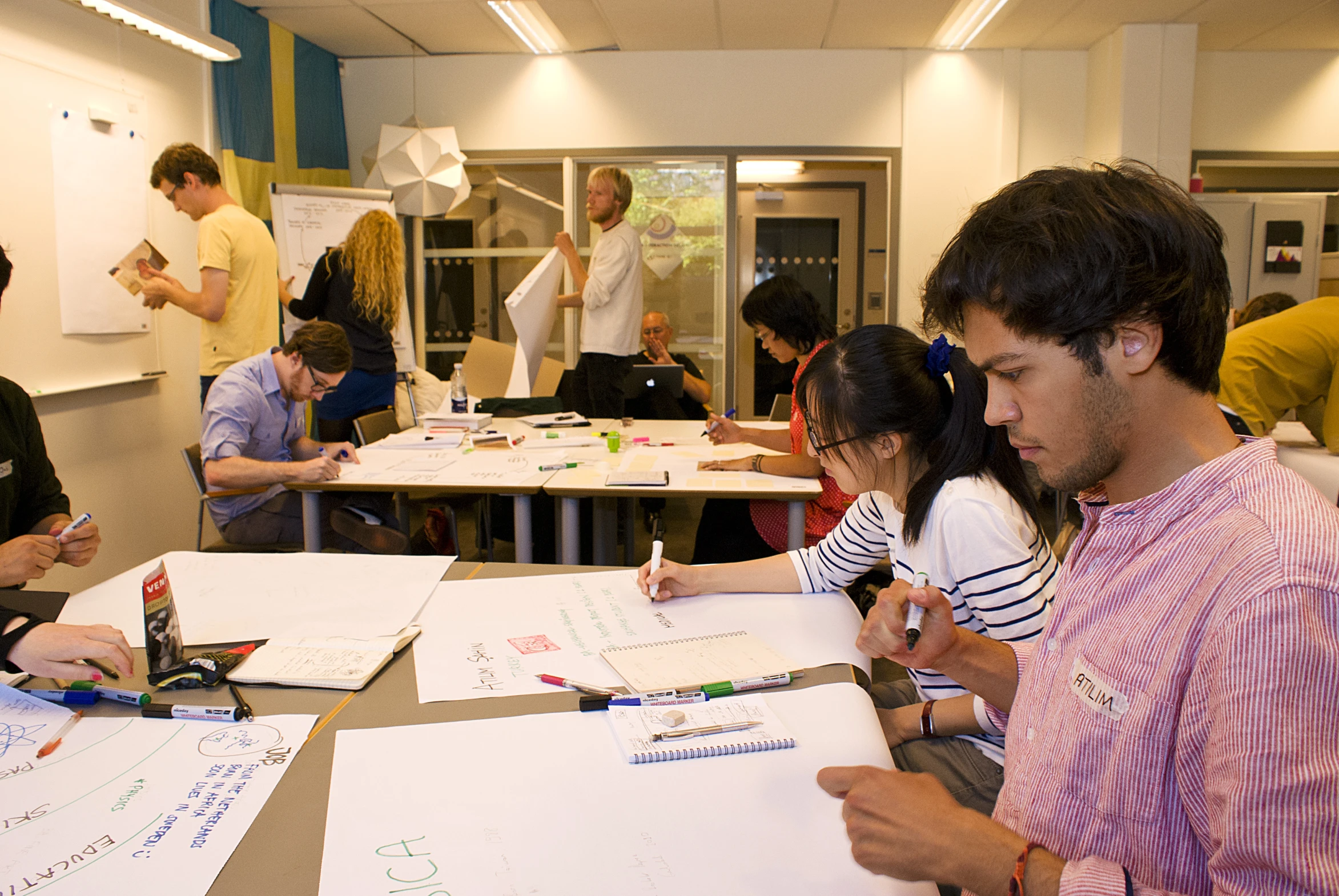 a group of people are sitting at a table in a room with markers and paper