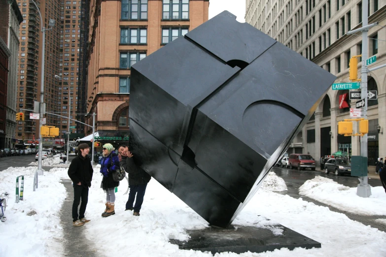 some people standing around in the snow by a giant black sculpture