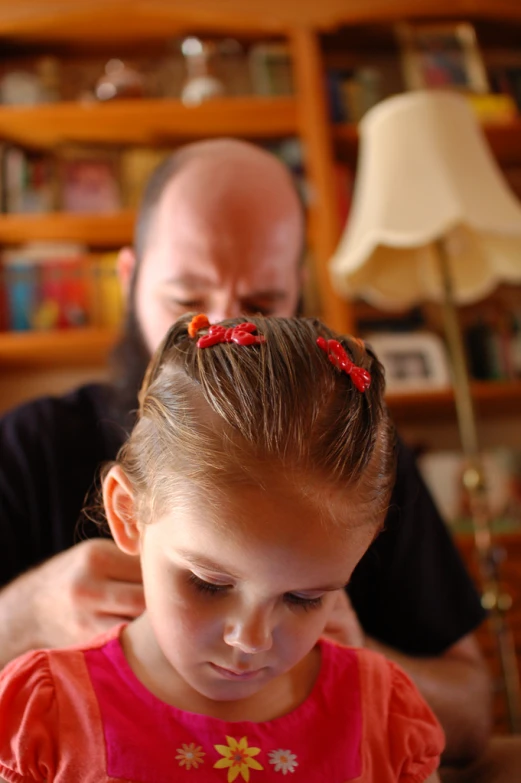 the man has the little girl's hair pulled up and looks down