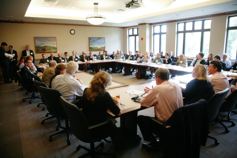 a big meeting in a huge conference room with people seated at the table listening