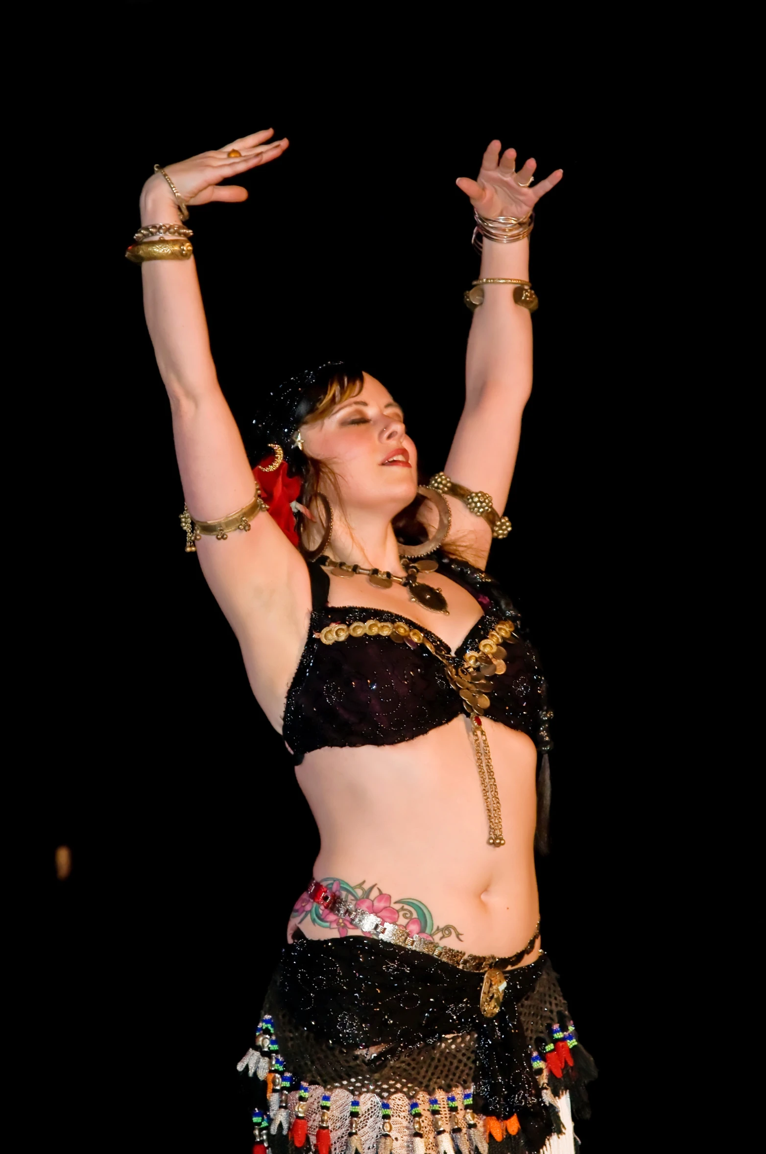 a belly dancer in black and gold with the other hands in the air