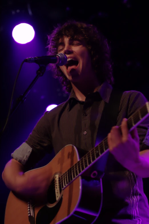 a young man sings into the microphone while playing his guitar