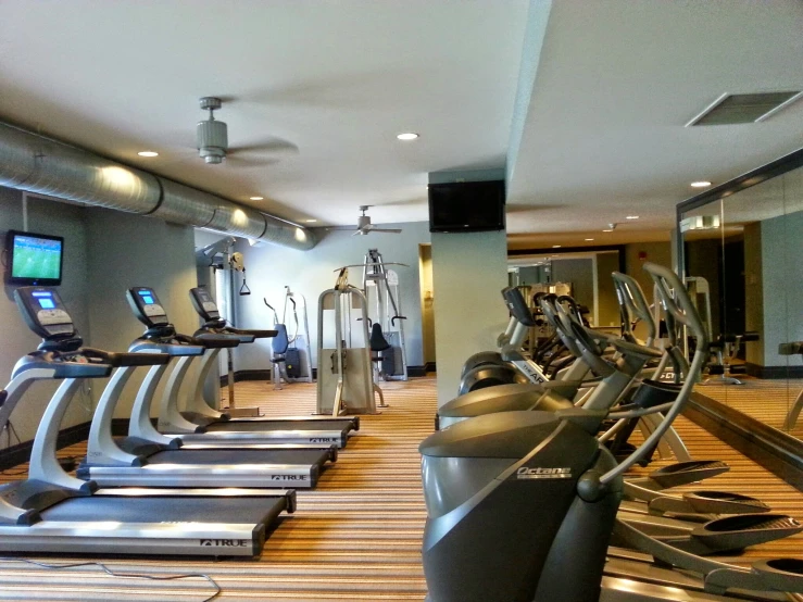 a row of treadmills are arranged in an empty room