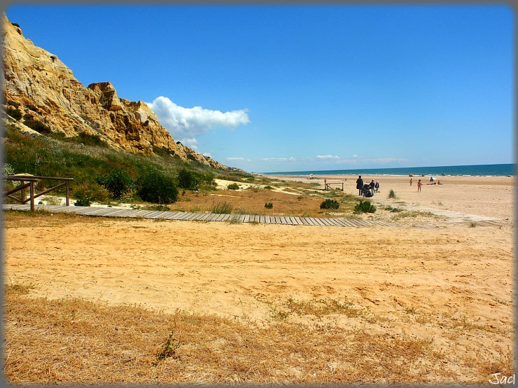 two people walk on the sandy beach by some mountains