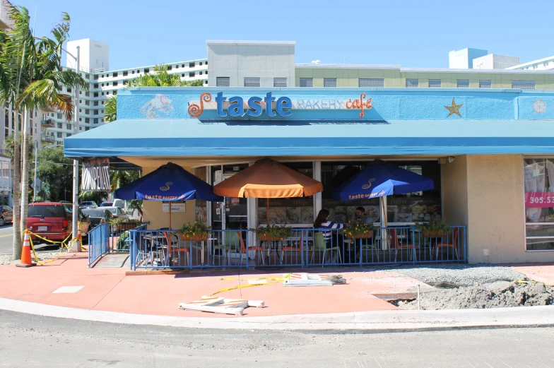 blue umbrellas and orange umbrella chairs outside of a small store