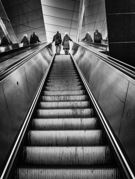 two people walk down an escalator and look at the floor