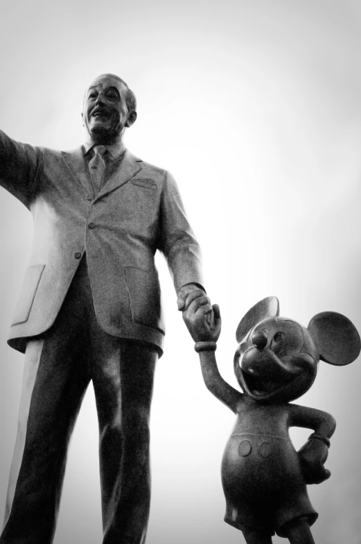 man in suit holding the hand of a statue of mickey mouse