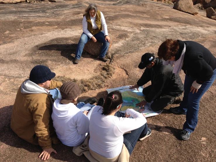 four people observing the map on top of a rock