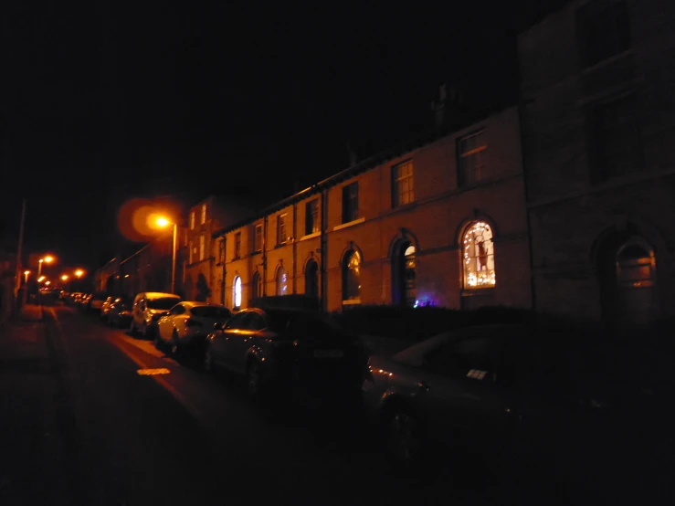 a dark street filled with parked cars next to a tall building