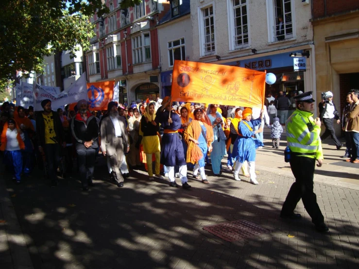 a crowd of people walk down a street holding orange and white signs
