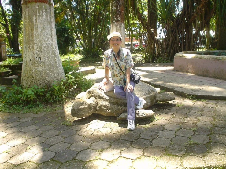 man wearing cap sitting on a rock with palm trees behind him