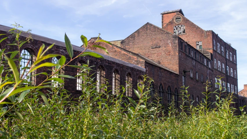 a large brown building with lots of windows next to green plants