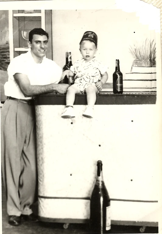 a man holding a  in his arms and a bottle of beer behind him