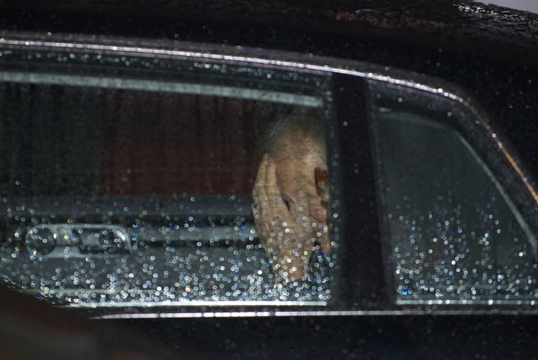 man in car looking out the window as rain falls