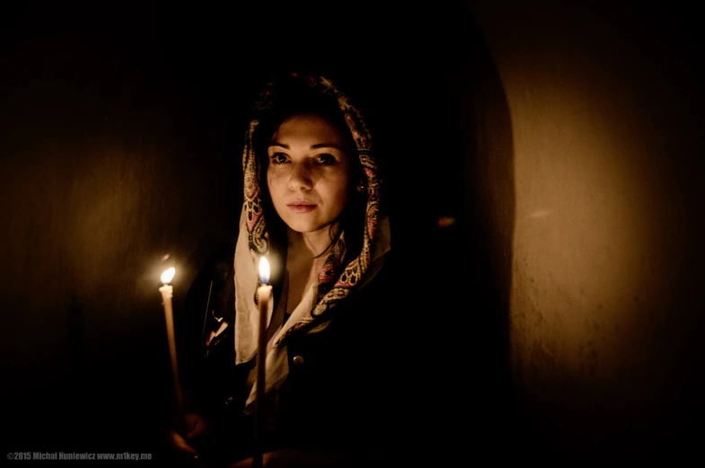 a woman standing in a dark room holding two candles