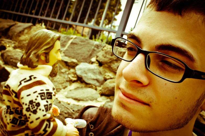 a boy with eyeglasses looking at a plastic doll