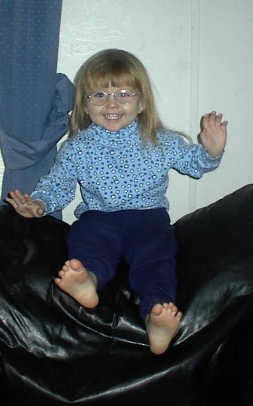 a small girl wearing glasses on a black couch