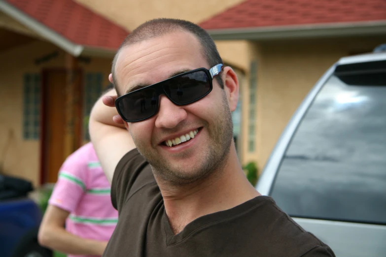 smiling man in black sunglasses with a pink woman standing behind him