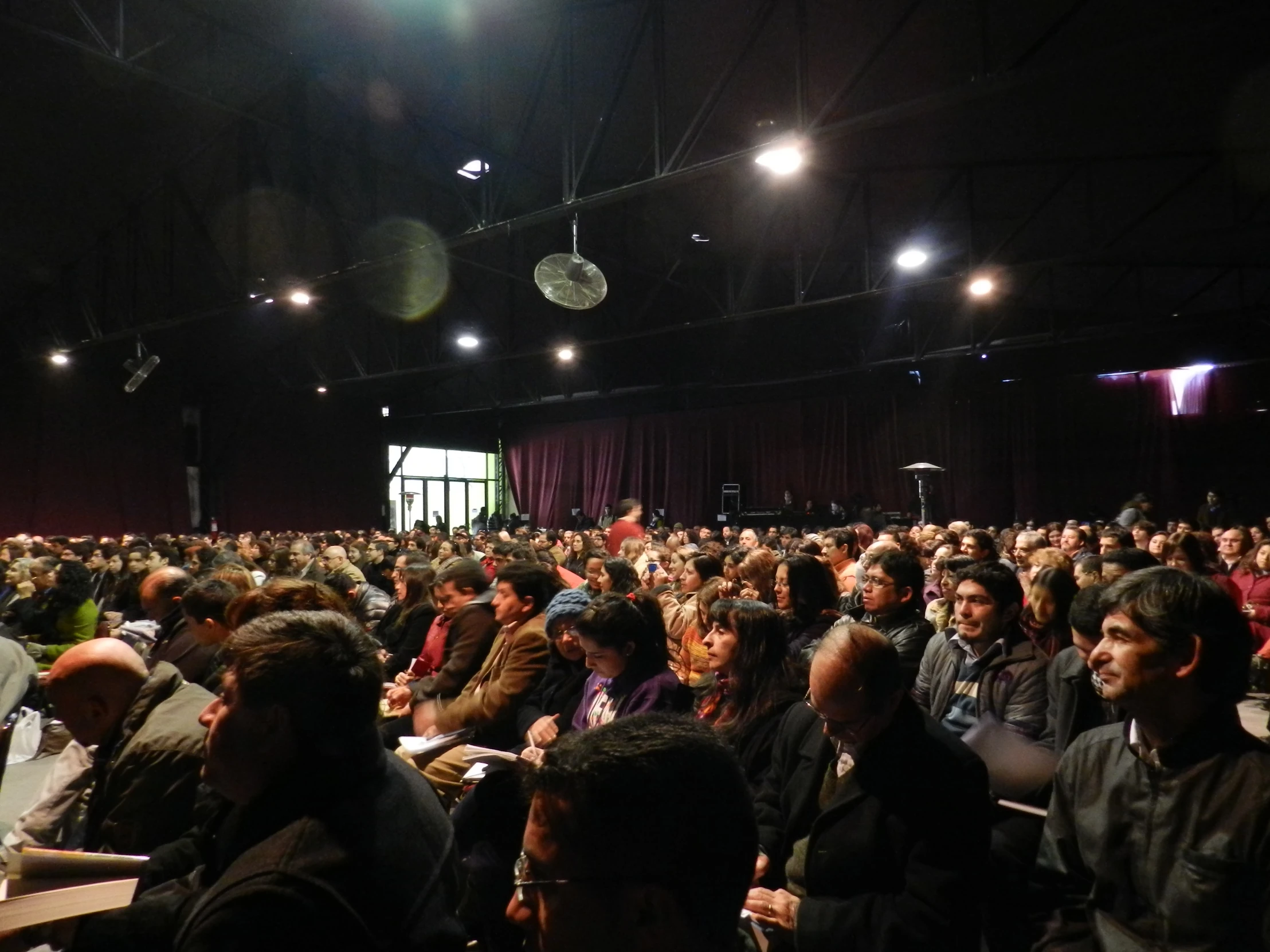 an audience at a conference hall, with a screen in the background