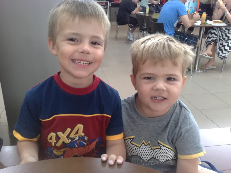 two boys sitting at a table with their faces turned