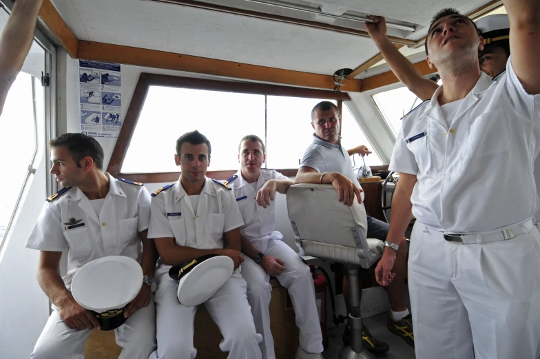 five men in white uniforms and other men in a row on a boat