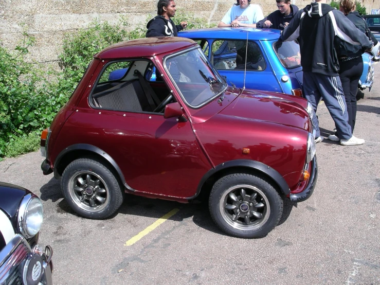 several people are standing around a small red car