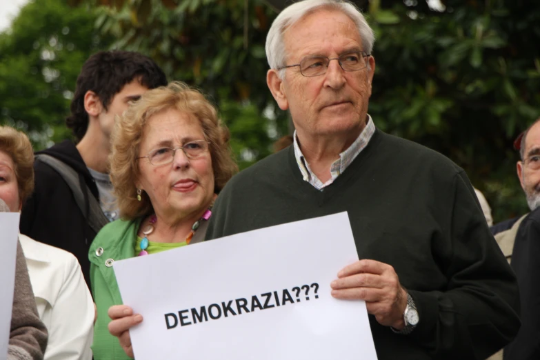 an older man is holding a sign while a woman and man stand behind him