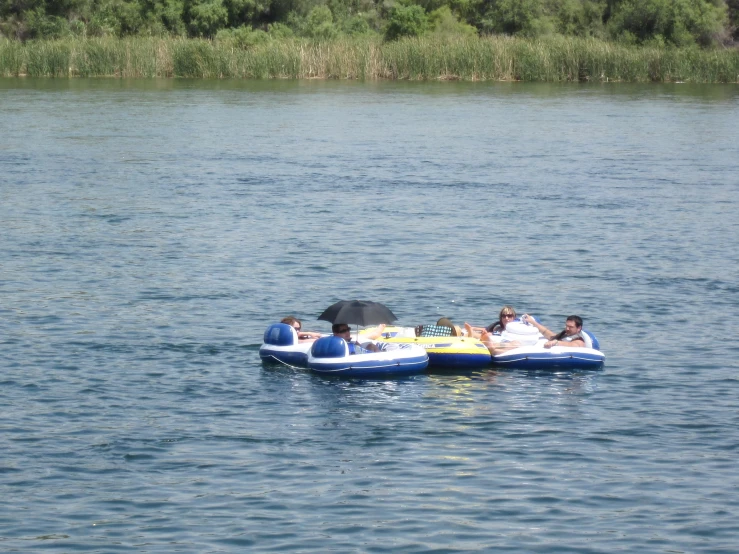 an inflatable raft is pulled by four s and an umbrella on a lake